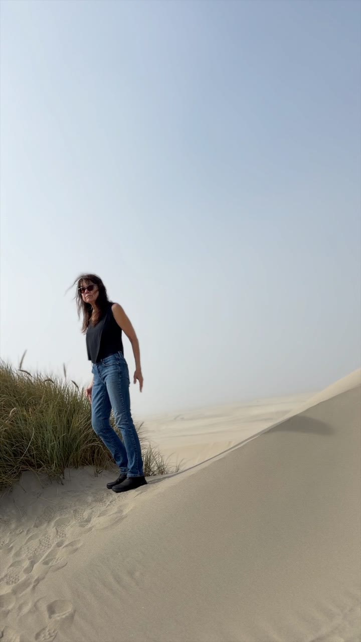 Jené Raél standing on a sand dune on the Oregon Coast